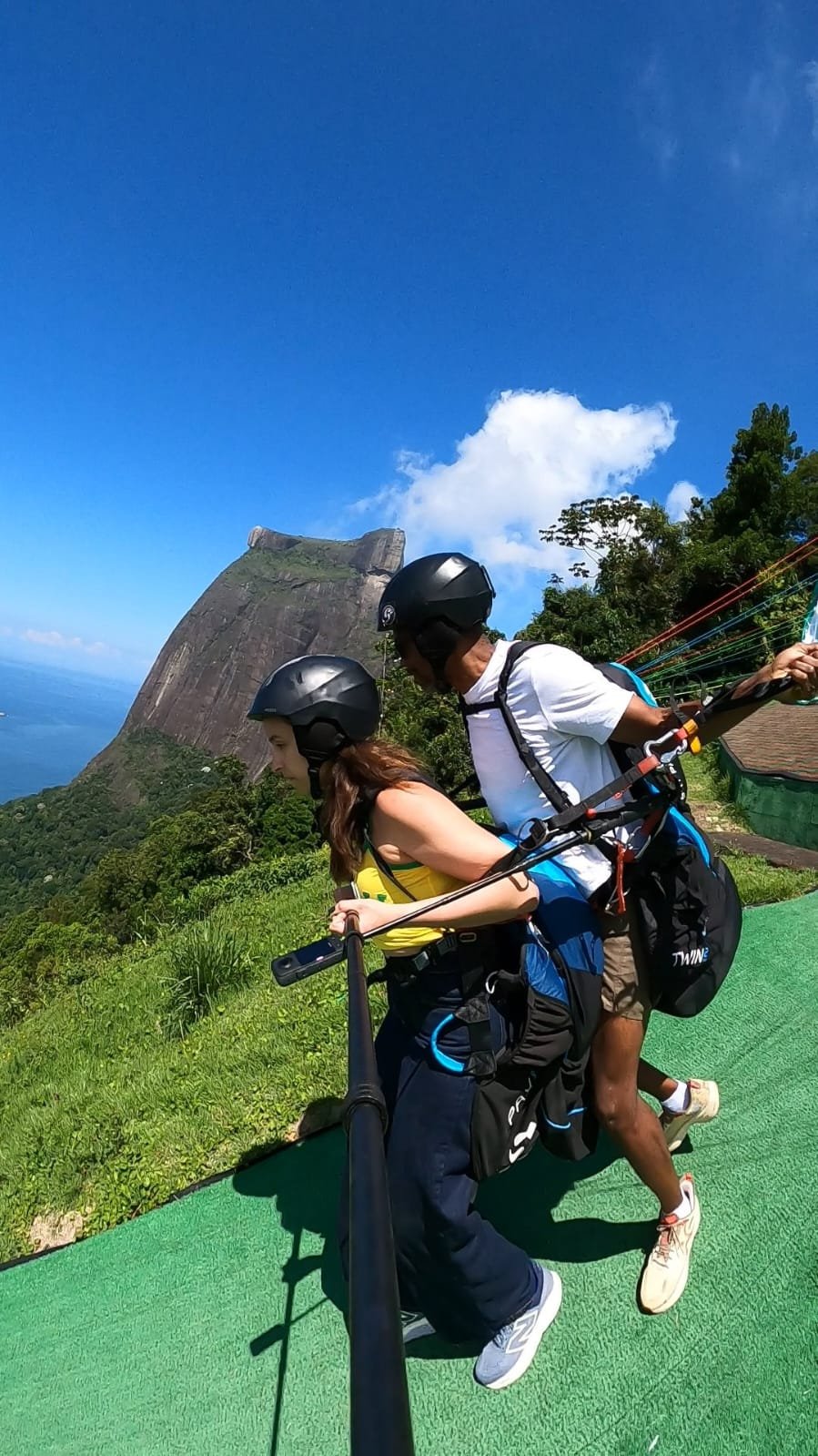 Instrutor e passageira na rampa de decolagem com as montanhas do Rio ao fundo